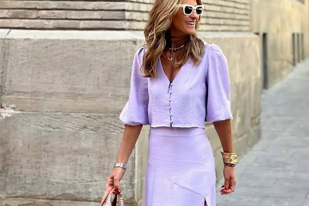 Kobieta w letniej stylizacji w odcieniu **kolor liliowy**. Krótka bluzka z bufiastymi rękawami i spódnica z rozcięciem.