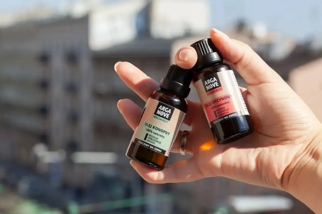 Dwie buteleczki olejków Arga Nove w dłoni. Dowiedz się, jak stosować olejek rycynowy na włosy dla ich regeneracji.