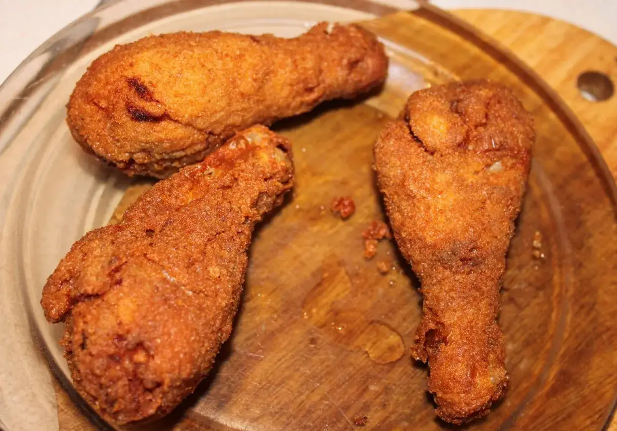 Trzy złociste, chrupiące pałki kurczaka na drewnianej desce.