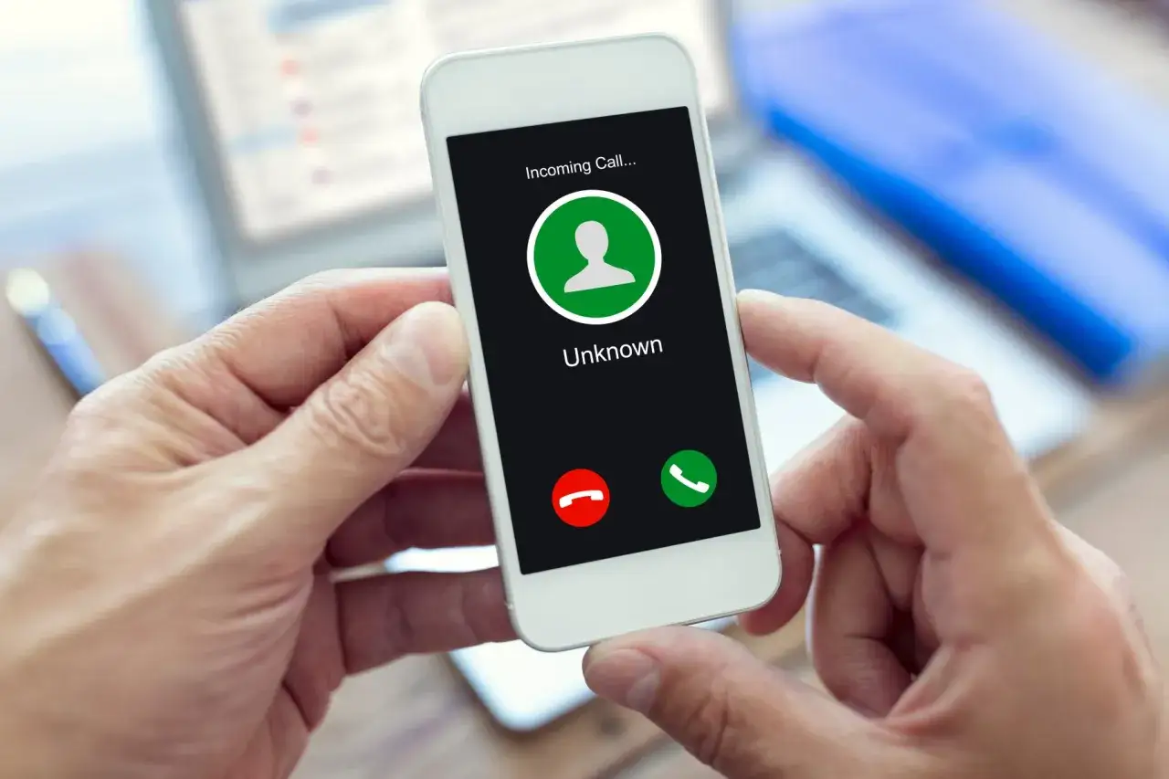 Dłoń trzyma smartfon z ekranem "Incoming Call... Unknown". Zastanawiasz się, jak ukryć swój numer?