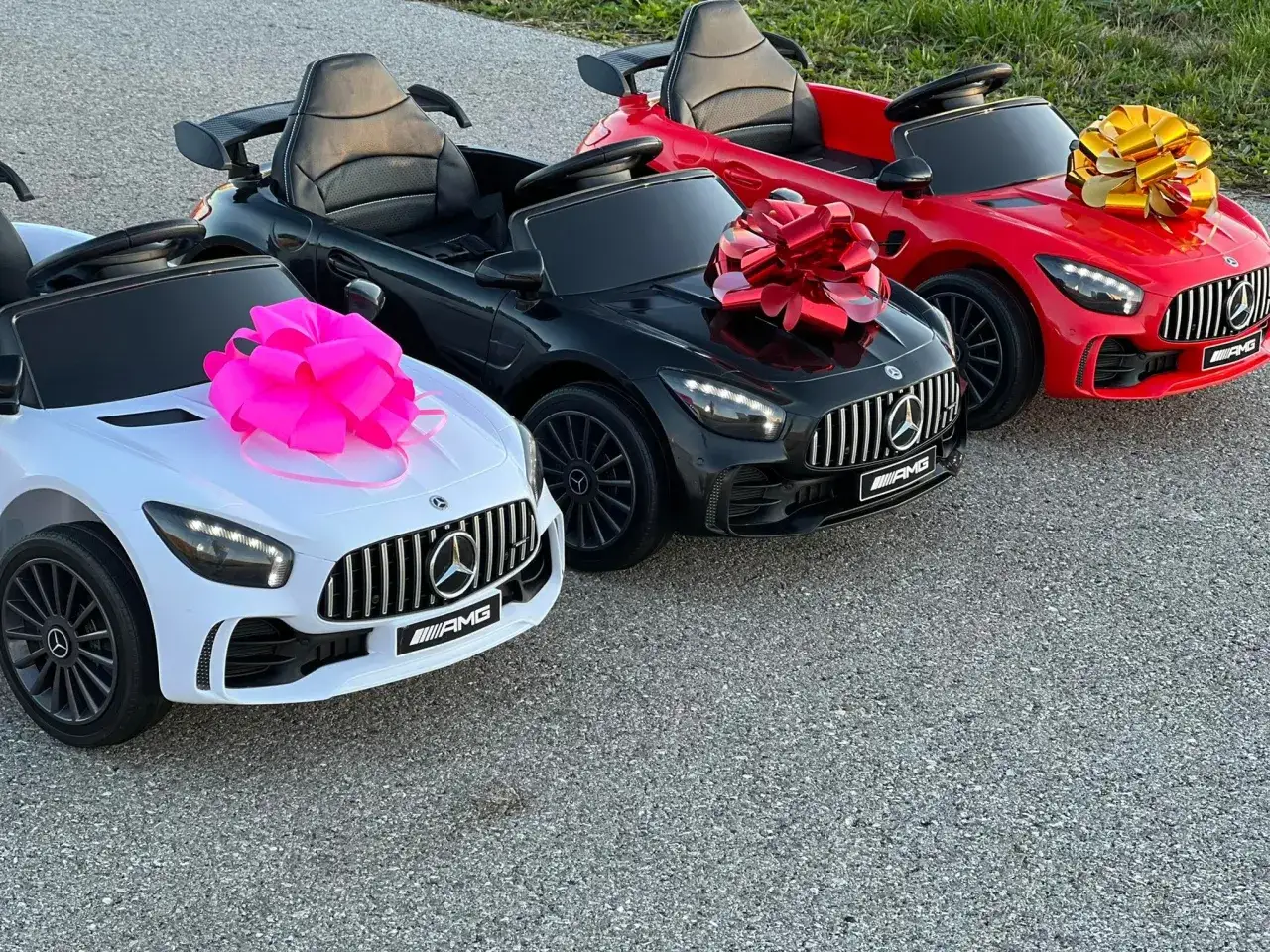 Trzy jeżdżące samochody dla dzieci w kolorach białym, czarnym i czerwonym, ozdobione kokardami.