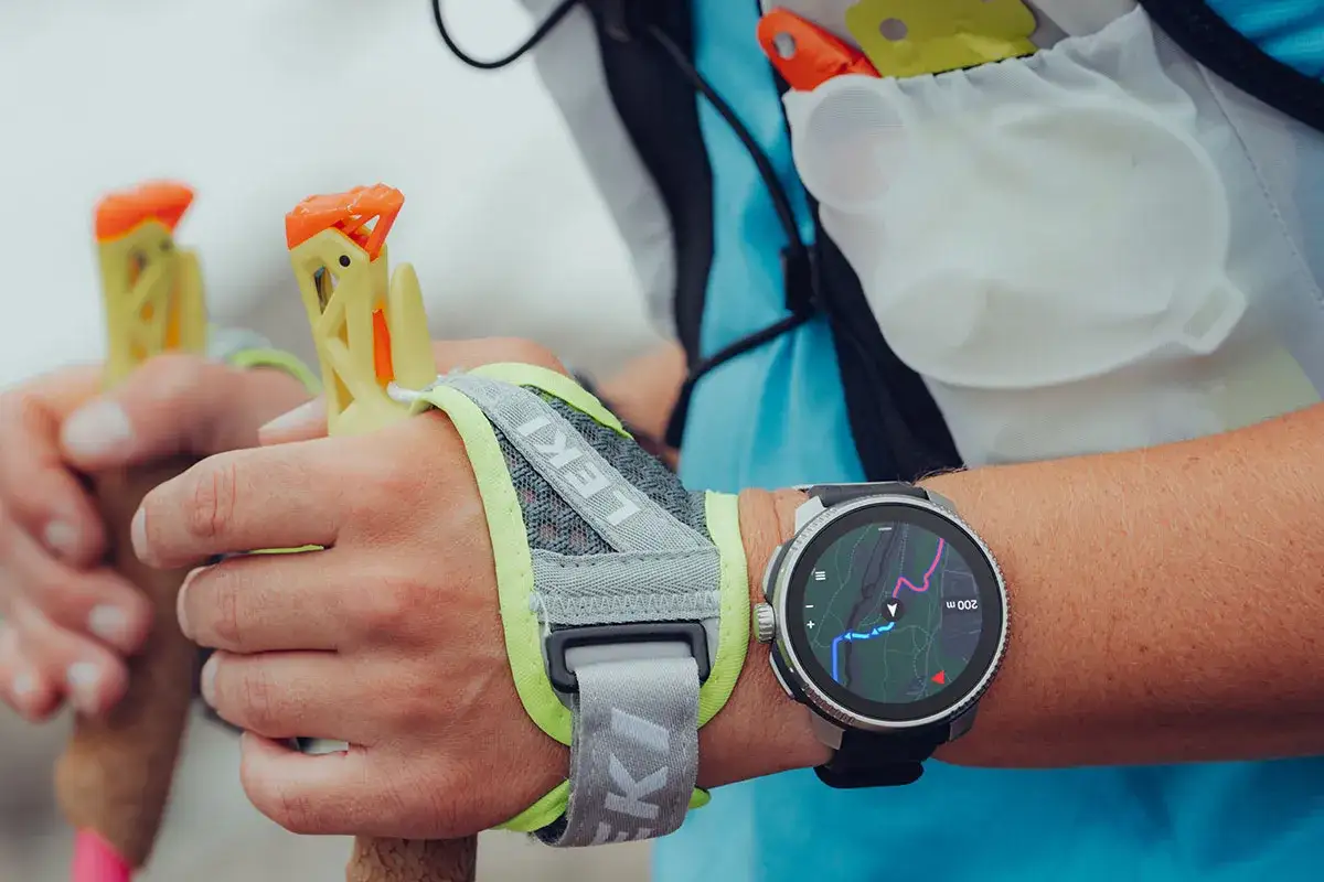 Zegarek z mapą szlaku na nadgarstku, idealny jako jaki zegarek w góry. Dłonie trzymają kijki trekkingowe Leki.