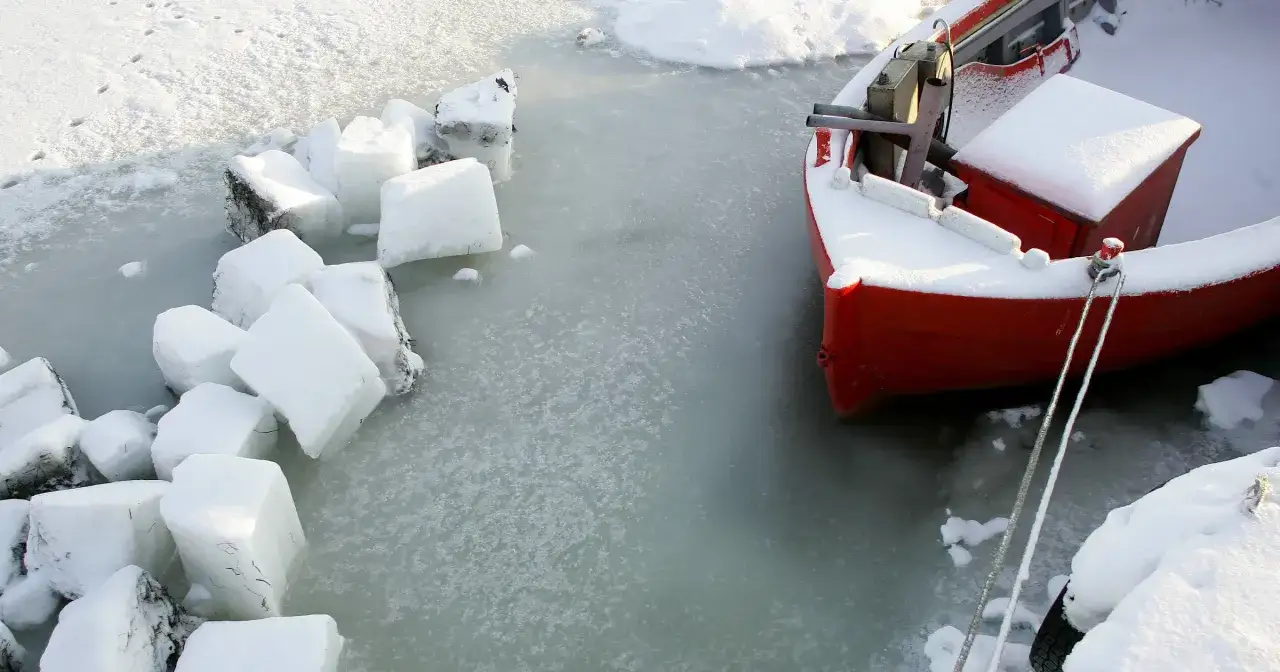Czerwona łódź przycumowana do zamarzniętej zatoki. Kiedy ostatnio zamarzła zatoka gdańska? Widać ślady na śniegu i bryły lodu.