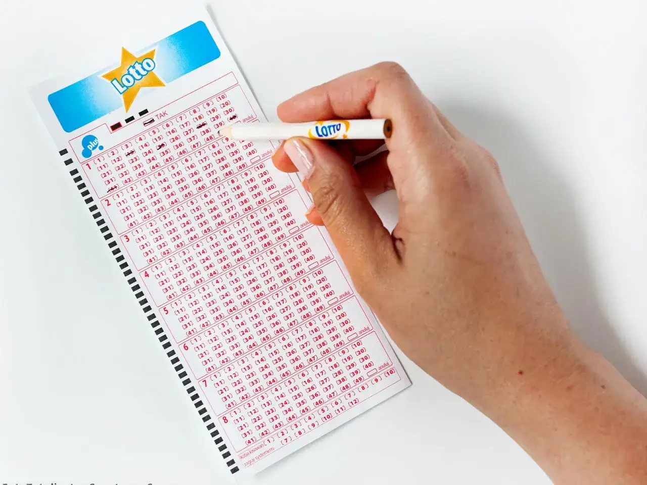 Dłoń z ołówkiem zaznacza liczby na kuponie Lotto. Zastanawiasz się, lotto ile jest do wygrania?