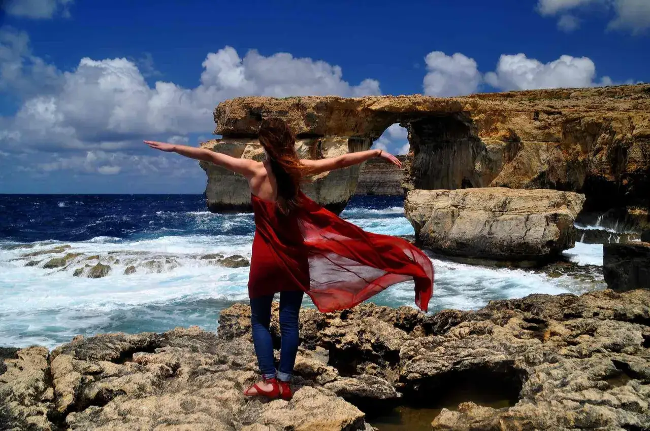 Kobieta w czerwonej sukience na Malcie, przy Azure Window. Idealne miejsce, by poczuć wiosnę, gdy zastanawiasz się, gdzie cieplej w kwietniu Cypr czy Malta.