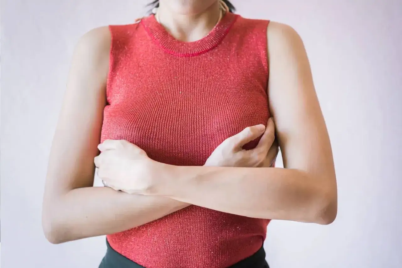 Kobieta w czerwonej bluzce obejmuje piersi. Czy to związane z prolaktyną? Co to jest prolaktyna?