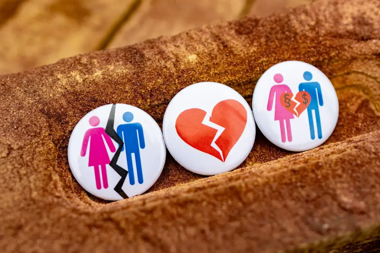 Trzy przypinki symbolizujące rozstanie: rozdzielona para, złamane serce i para z paragrafem i dolarem. Symbolizują wspólny pozew o rozwód bez orzekania o winie.