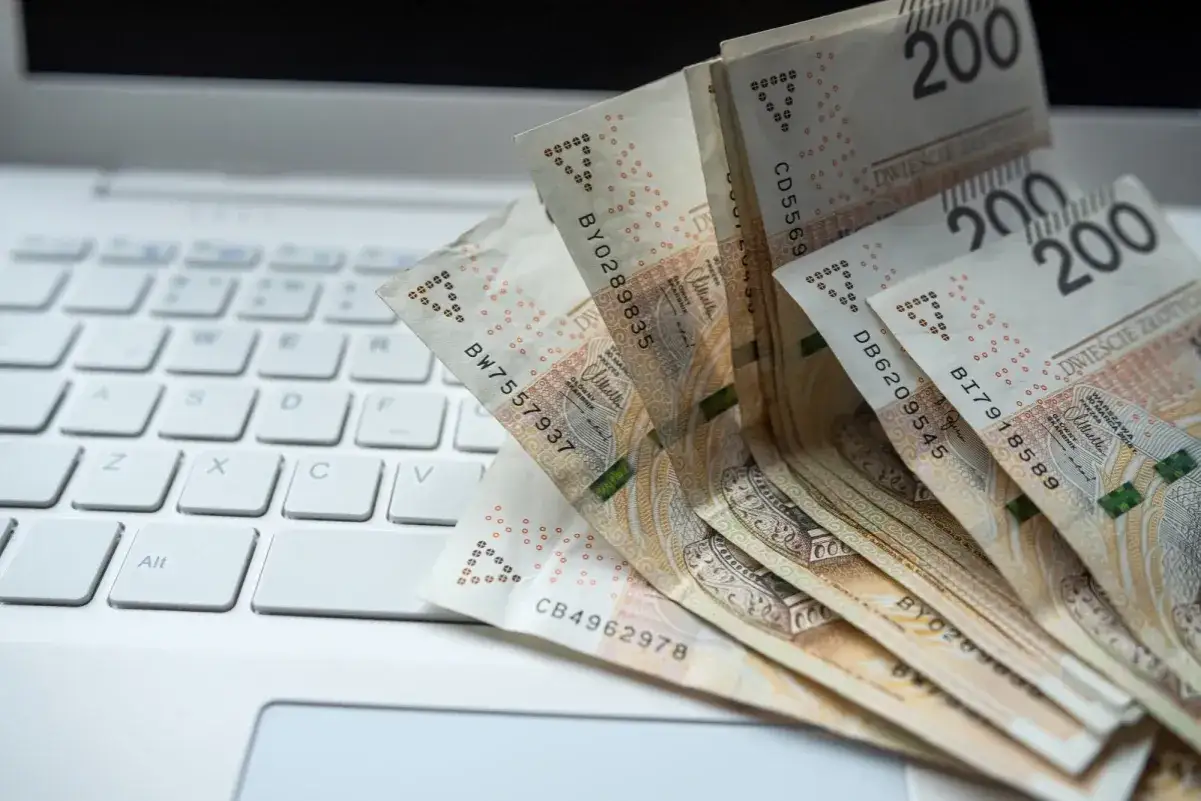 Banknoty 200 zł leżące na białej klawiaturze laptopa.