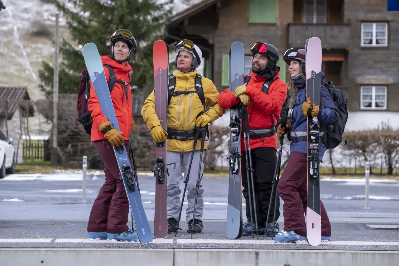 Cztery osoby w strojach narciarskich stoją z nartami.
