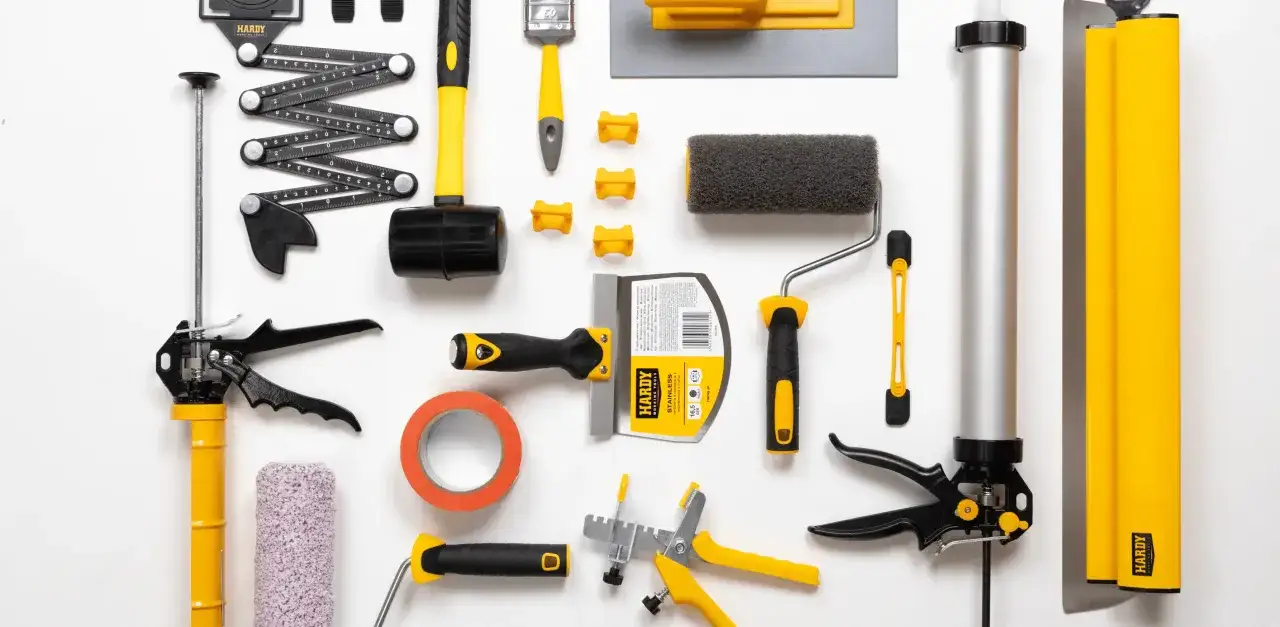 Zestaw podstawowych narzędzi stolarskich: młotek gumowy, paca, wałek, pędzel, taśma, pistolet do silikonu i inne.