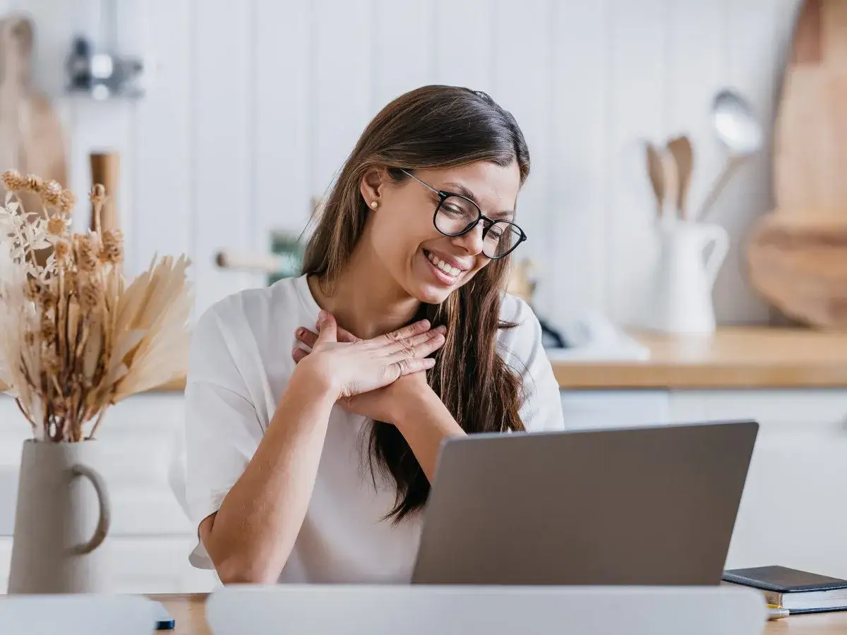 Uśmiechnięta kobieta z dłońmi na sercu, jakby czytała inspirujące cytaty o podziękowaniu.
