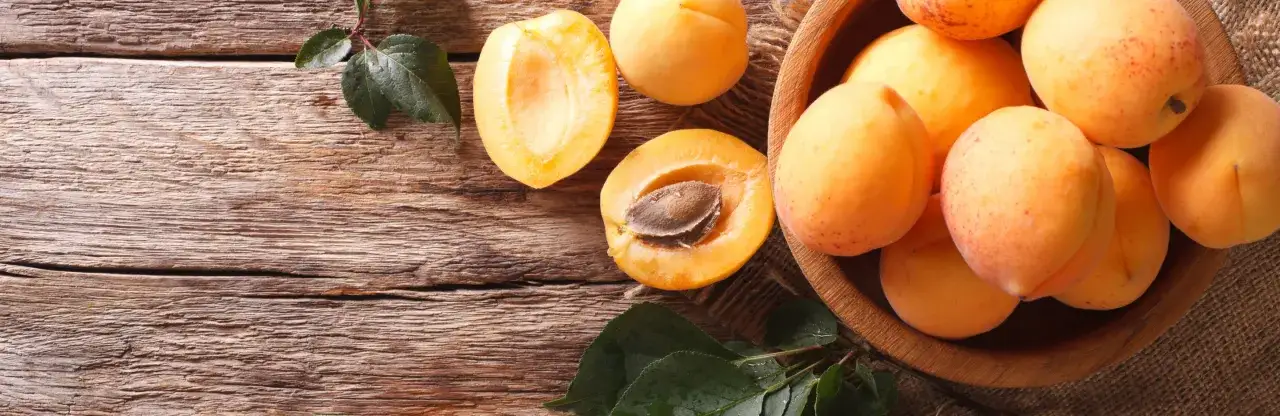 Dojrzałe morele w drewnianej misie i połówki owoców na drewnianym blacie. Zastanawiasz się, po ilu latach owocuje morela?