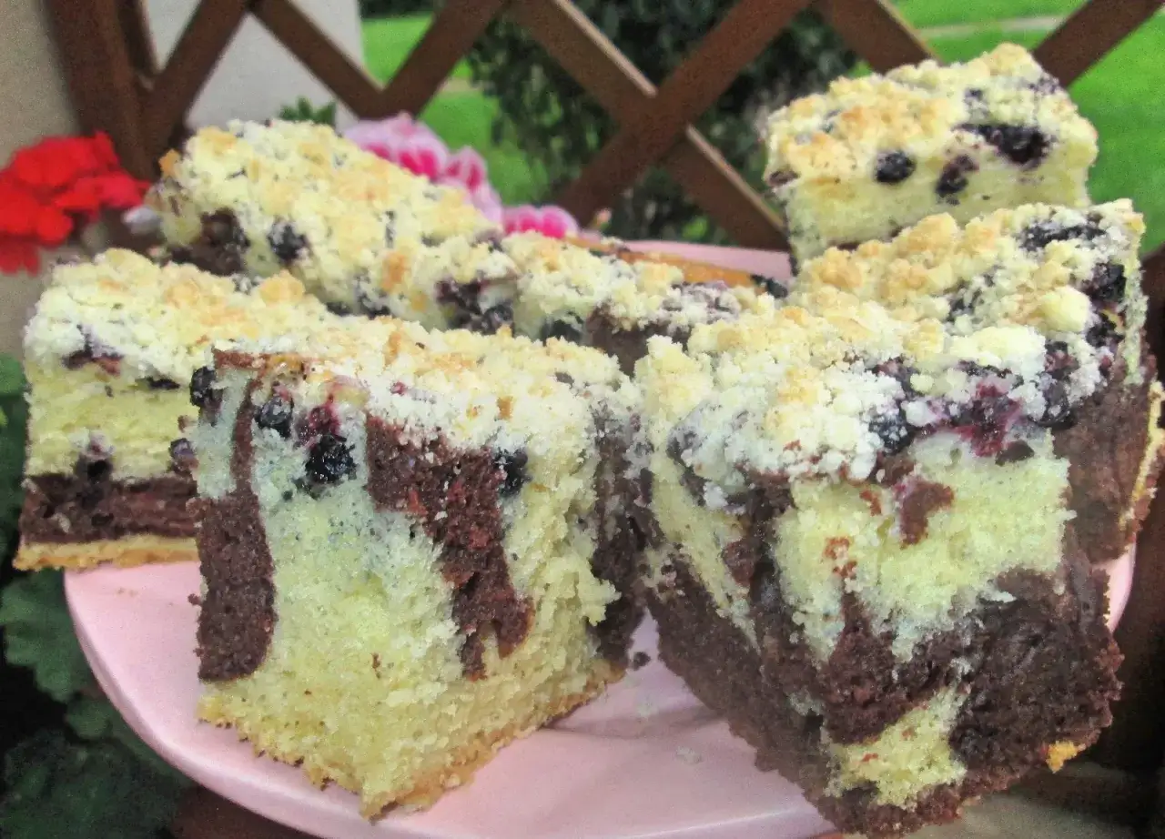 Pyszny biszkopt z jagodami i kruszonką, z czekoladowymi smugami, na różowym talerzu.