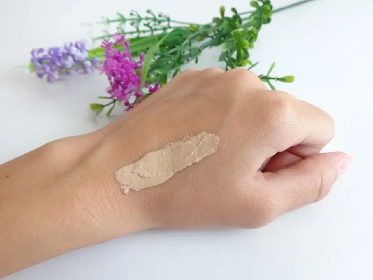 Próbka kremu BB na dłoni, obok kwiatów.