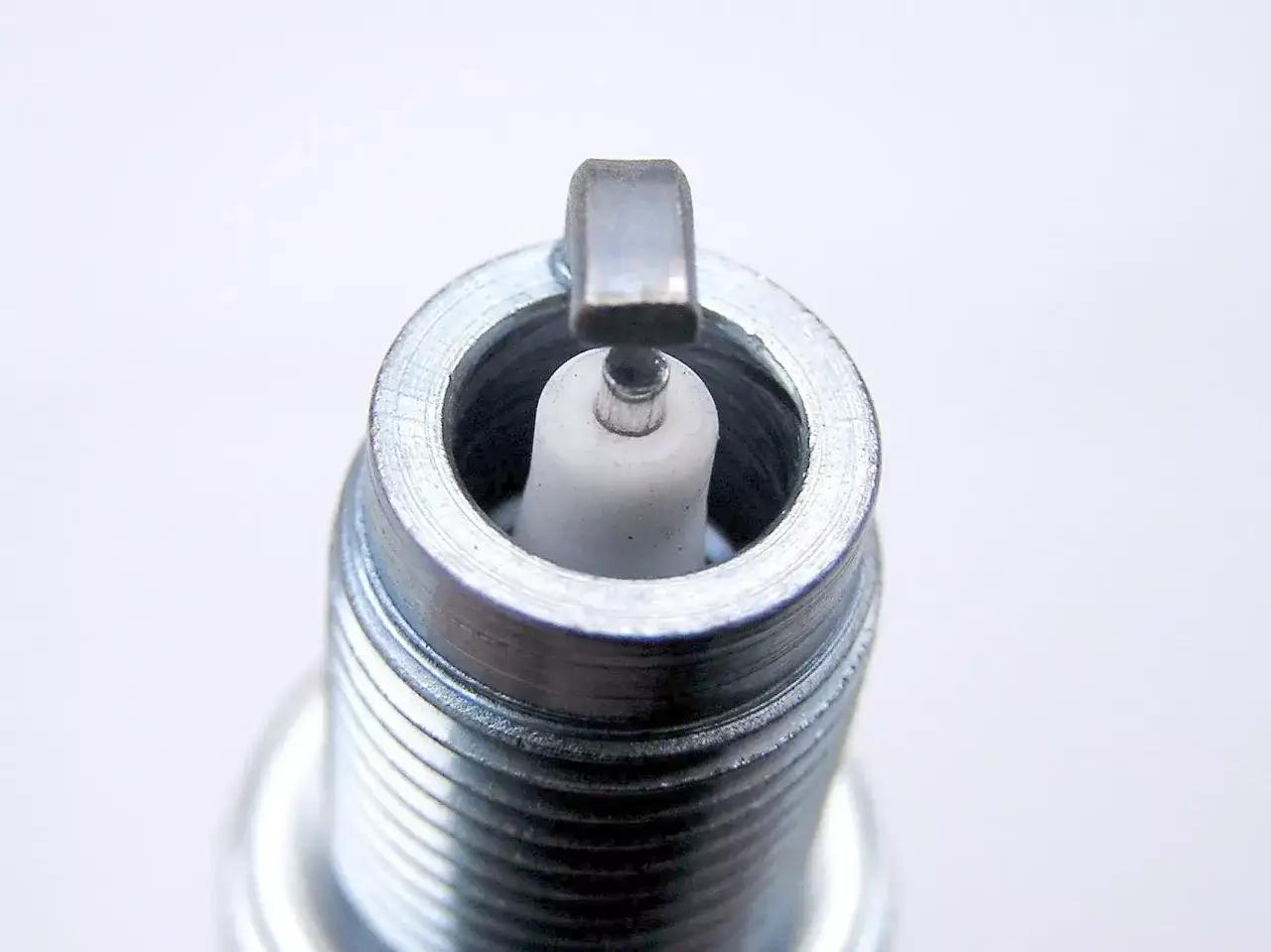 Zbliżenie na końcówkę świecy zapłonowej z białym izolatorem i metalową elektrodą.
