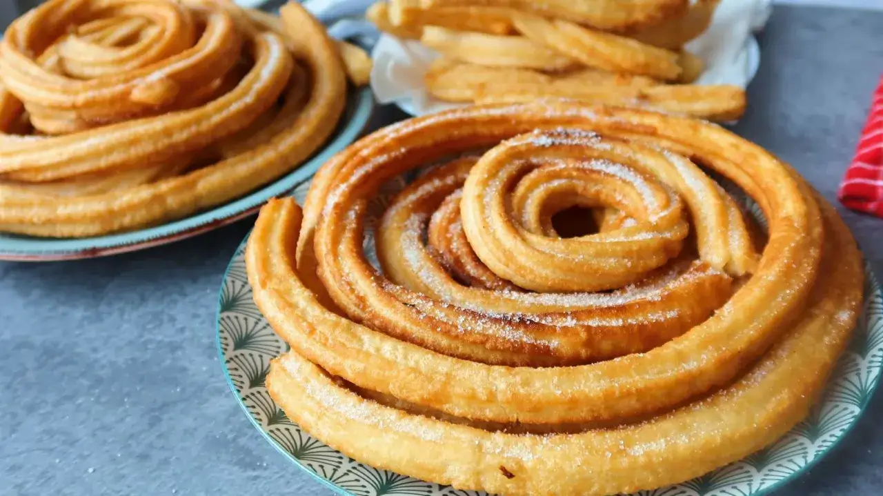Churros dorados y azucarados en espiral en platos.