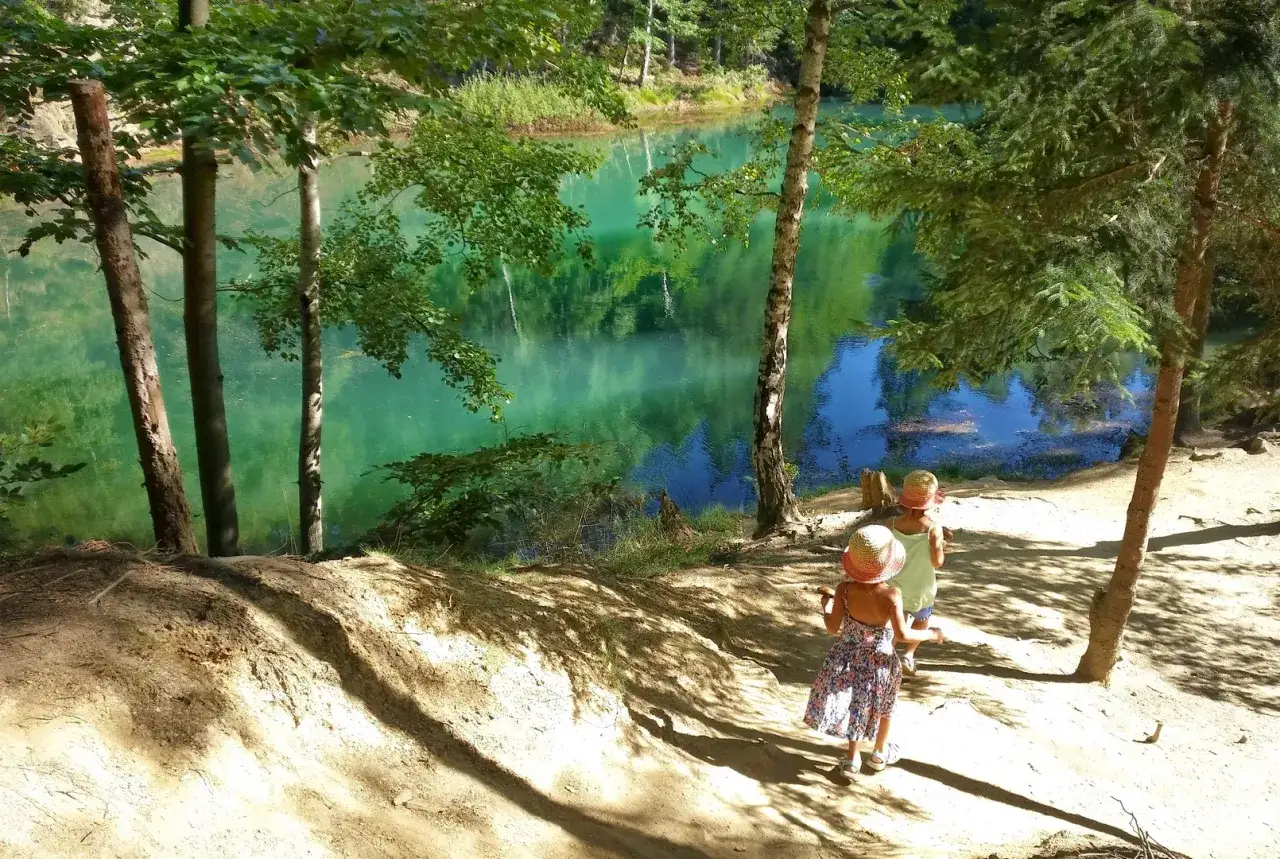 Dwie dziewczynki w słomkowych kapeluszach idą ścieżką nad turkusowe jezioro. Idealne miejsce, w jakie góry z dziećmi na letnią przygodę.