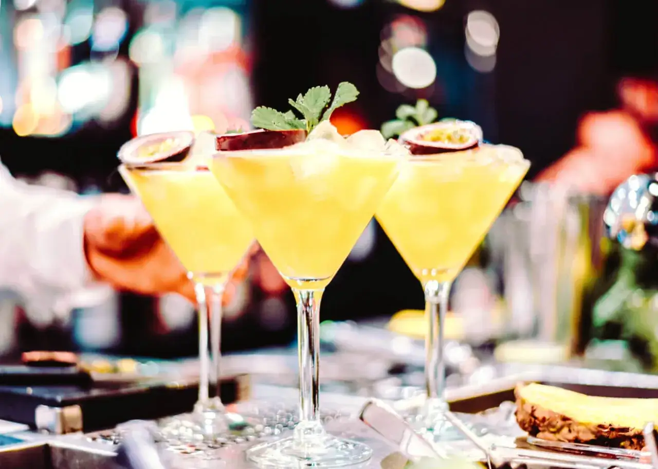 Trzy kieliszki z orzeźwiającą mango margarita, ozdobione połówkami marakui i listkami mięty, gotowe do podania.