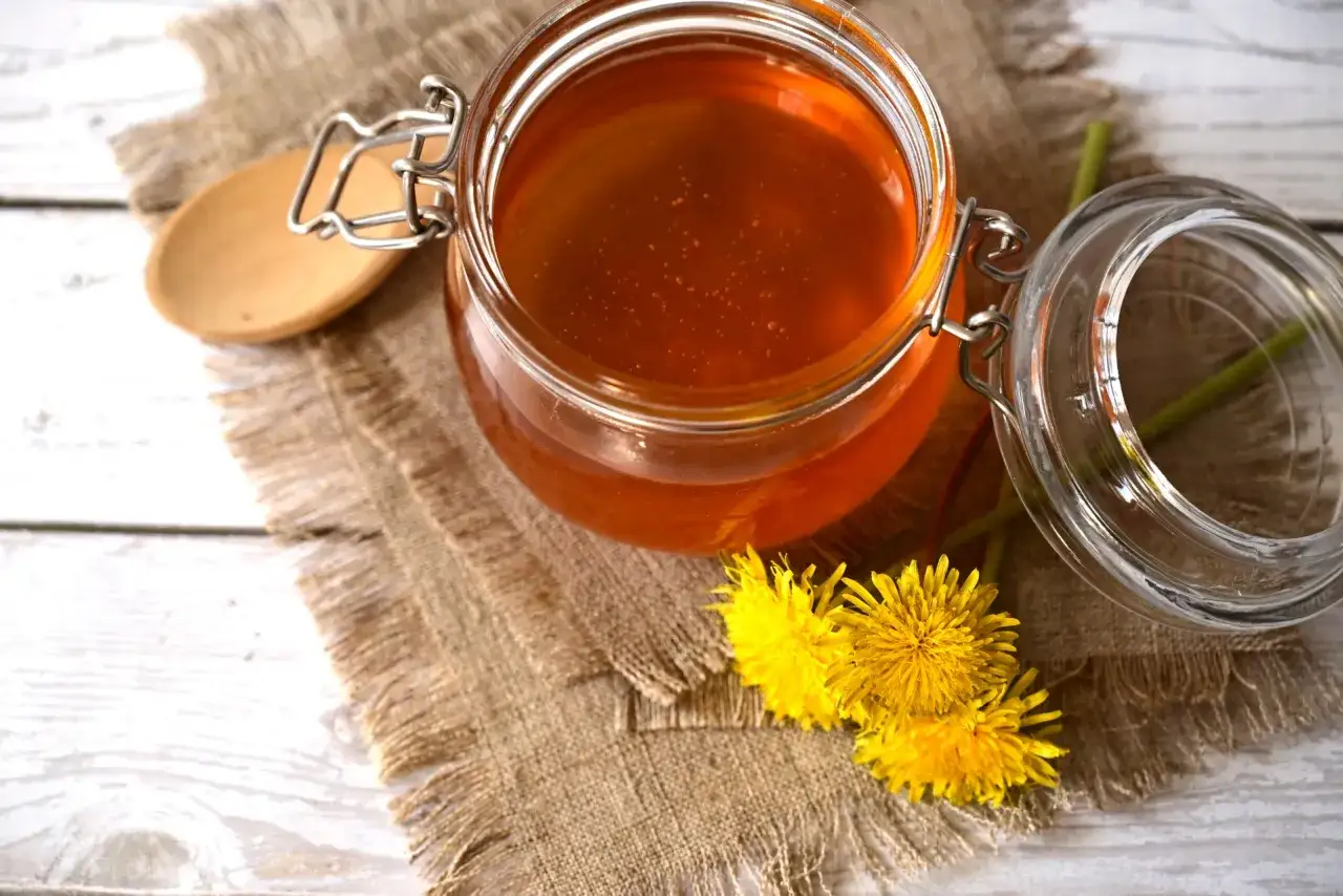 Słoik pełen złotego syropu z mniszka, obok świeże kwiaty.