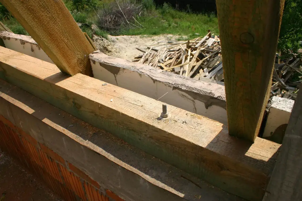 Drewniane belki konstrukcyjne, widoczna impregnacja drewna, przygotowane do budowy dachu.