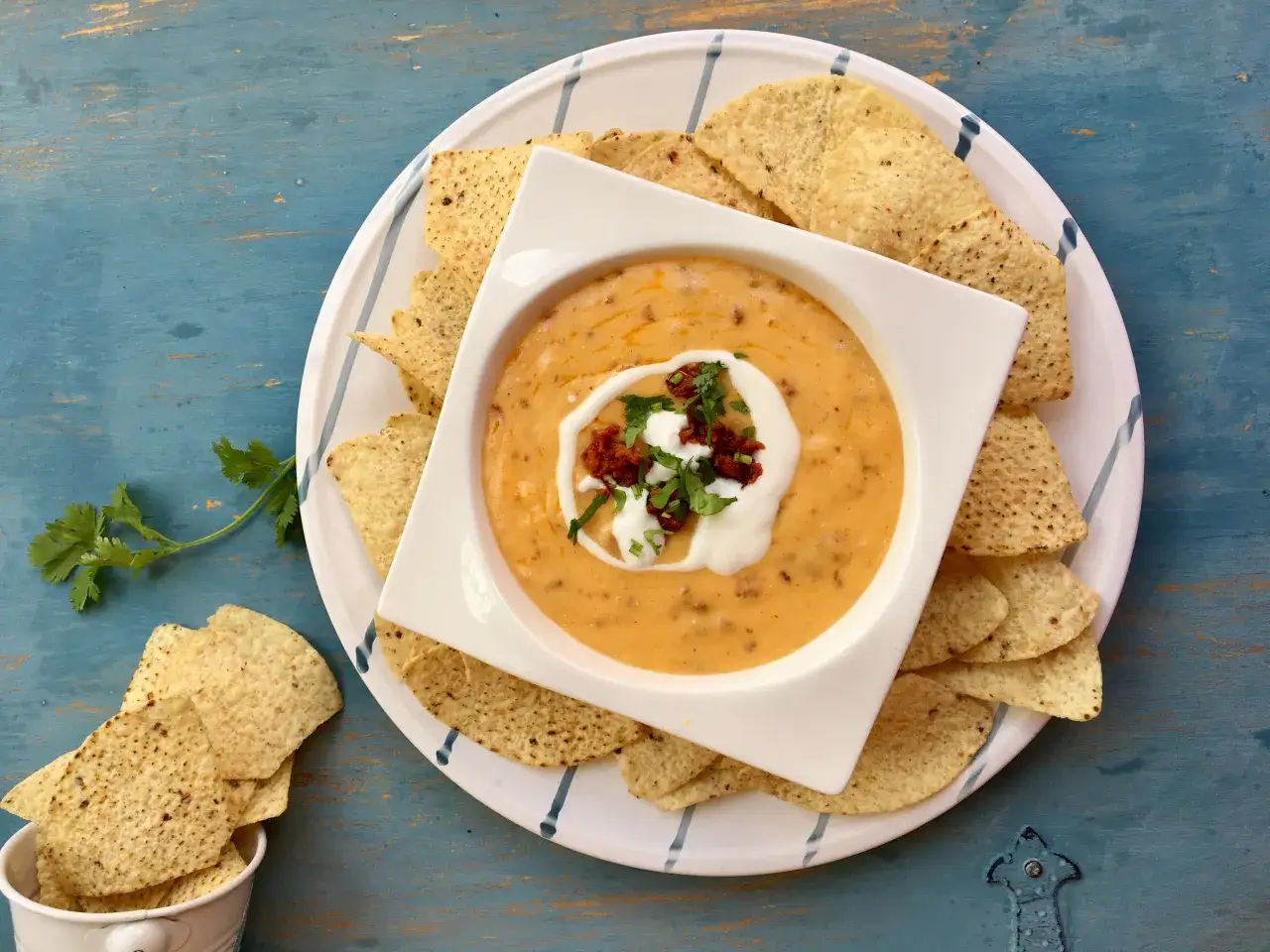 Salsa de queso cremosa en un tazón blanco, rodeada de totopos y adornada con crema y cilantro.