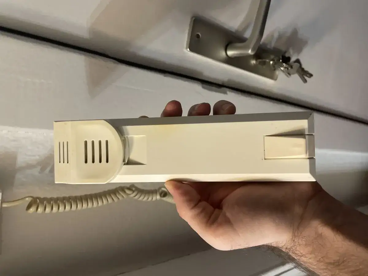 Dłoń trzymająca domofon. Zastanawiasz się, jak wyłączyć dźwięk w domofonie? Ten model ma przycisk z boku.