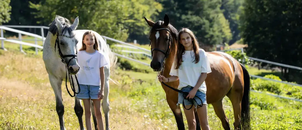 Dwie dziewczynki stoją obok koni na łące.
