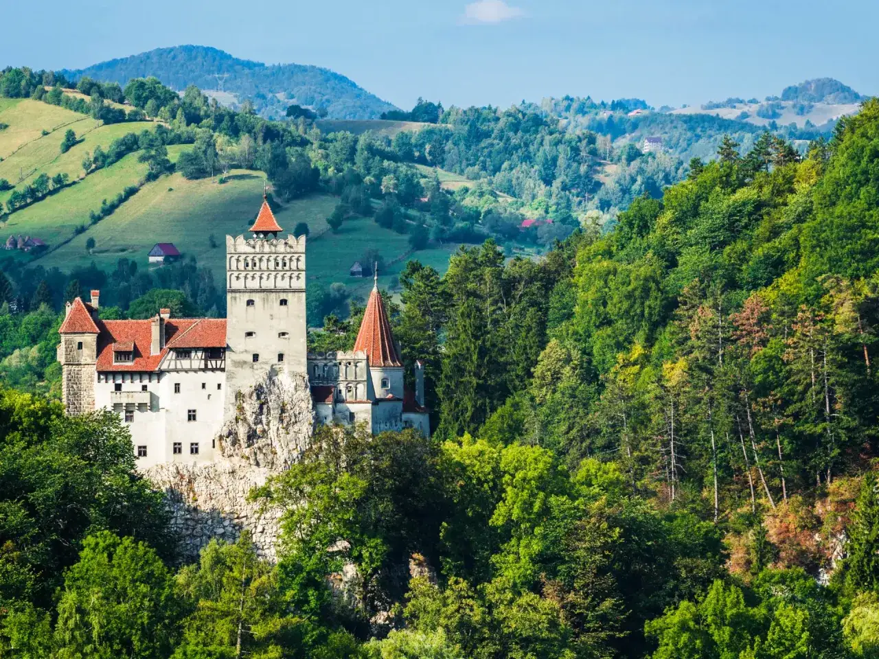 Zamek Bran w Rumunii na tle zielonych wzgórz i lasów.