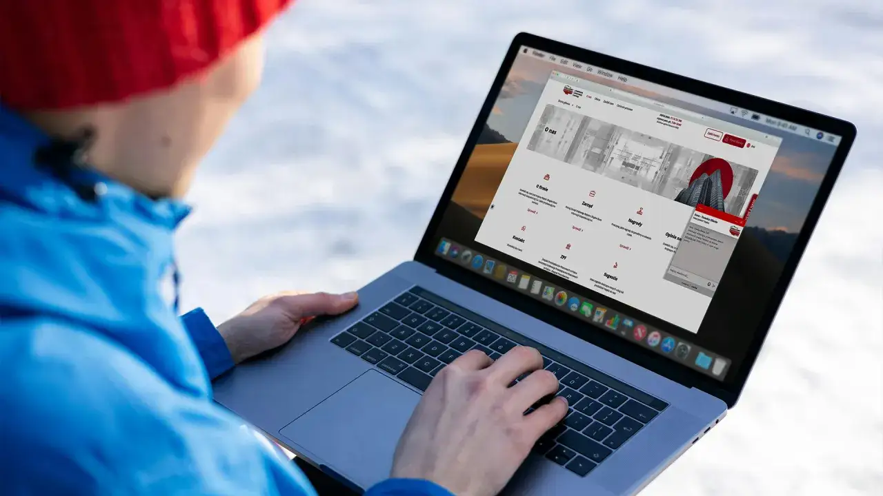 Osoba w czerwonej czapce i niebieskiej kurtce korzysta z laptopa, na ekranie którego widoczna jest strona internetowa KRD.