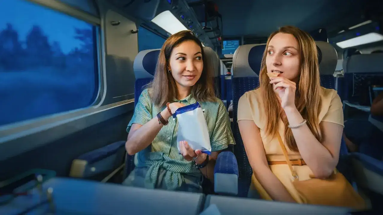 Dwie kobiety jedzą przekąski w pociągu intercity, patrząc przez okno.
