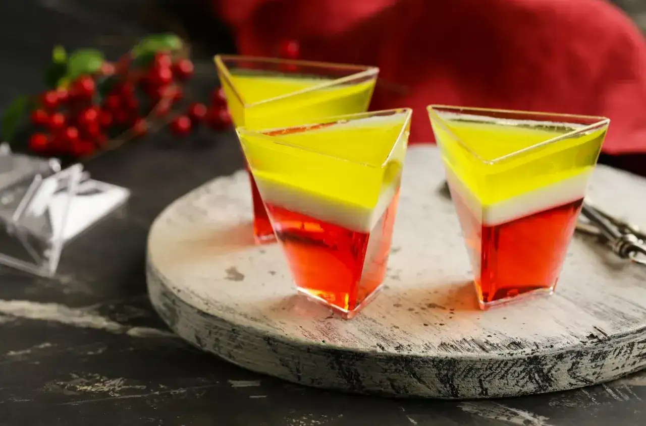 Trzy warstwowe galaretki w przezroczystych pucharkach na desce, ozdobione czerwonymi owocami.