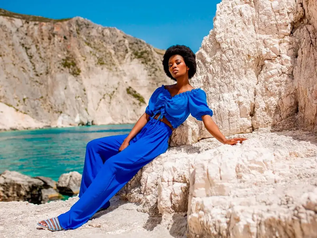 Modelka w niebieskim komplecie, idealna odpowiedź na pytanie: jaka bluzka do niebieskich spodni? Wakacyjny look na tle skalistej plaży.