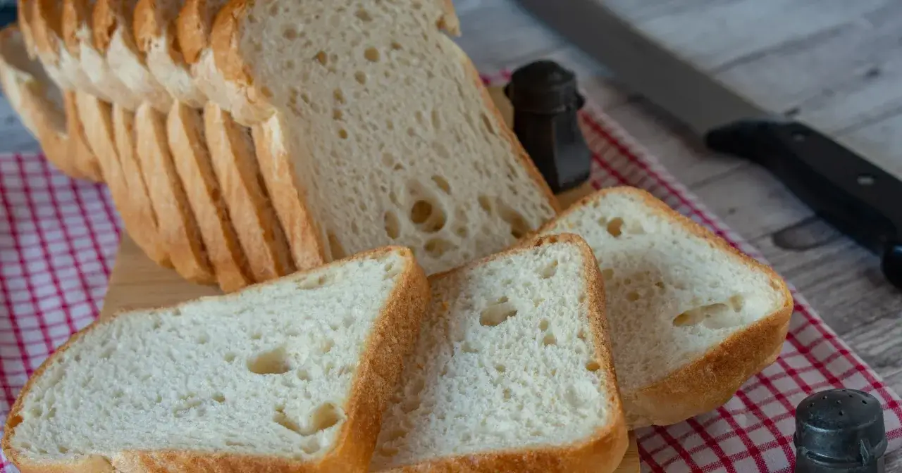 Pokrojony domowy chleb bezglutenowy na desce, obok solniczka i nóż.
