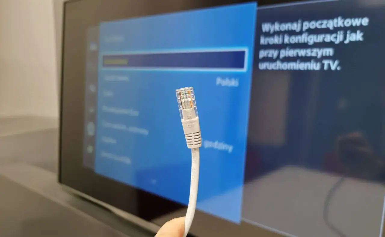 Kabel sieciowy Ethernet zbliżenie na wtyczkę RJ45 na tle ekranu telewizora z menu ustawień.