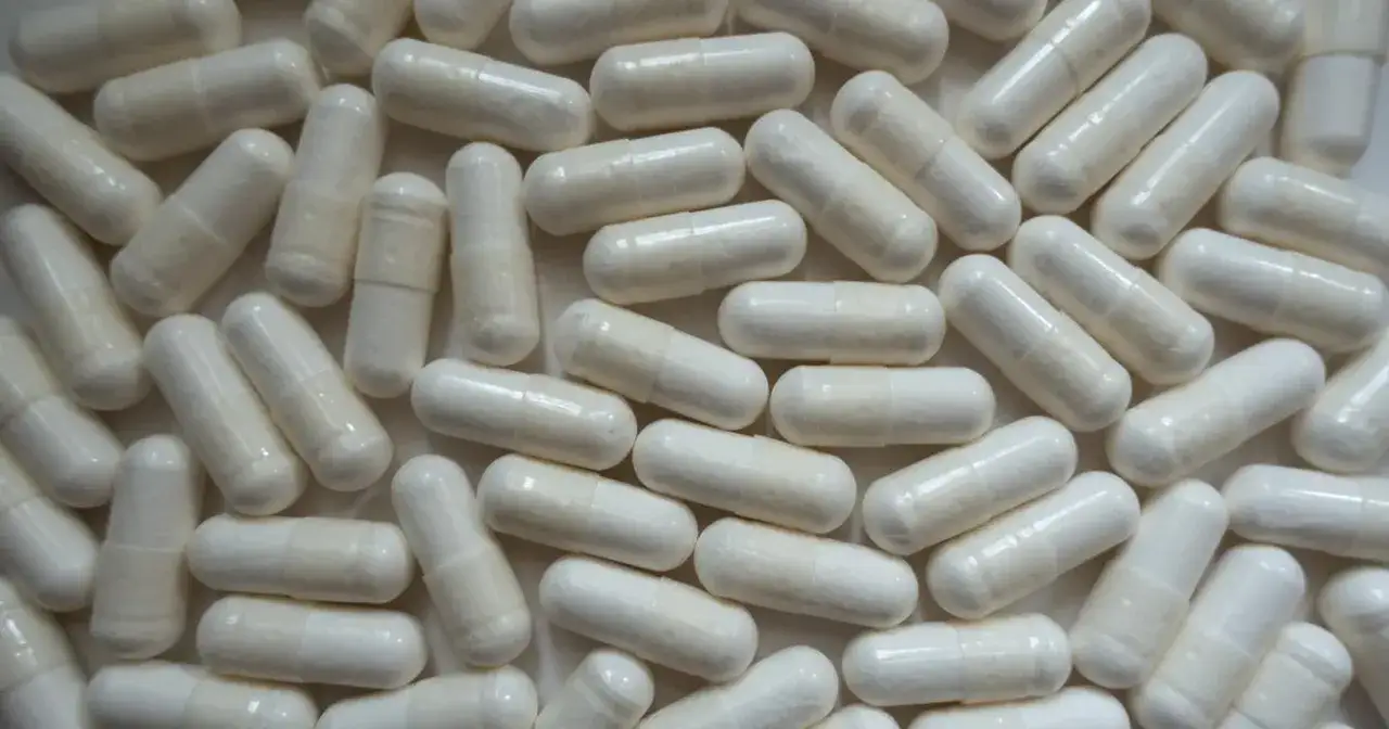 Mnóstwo białych kapsułek z cytrynianem magnezu, które pomagają w regeneracji i wspierają zdrowie.
