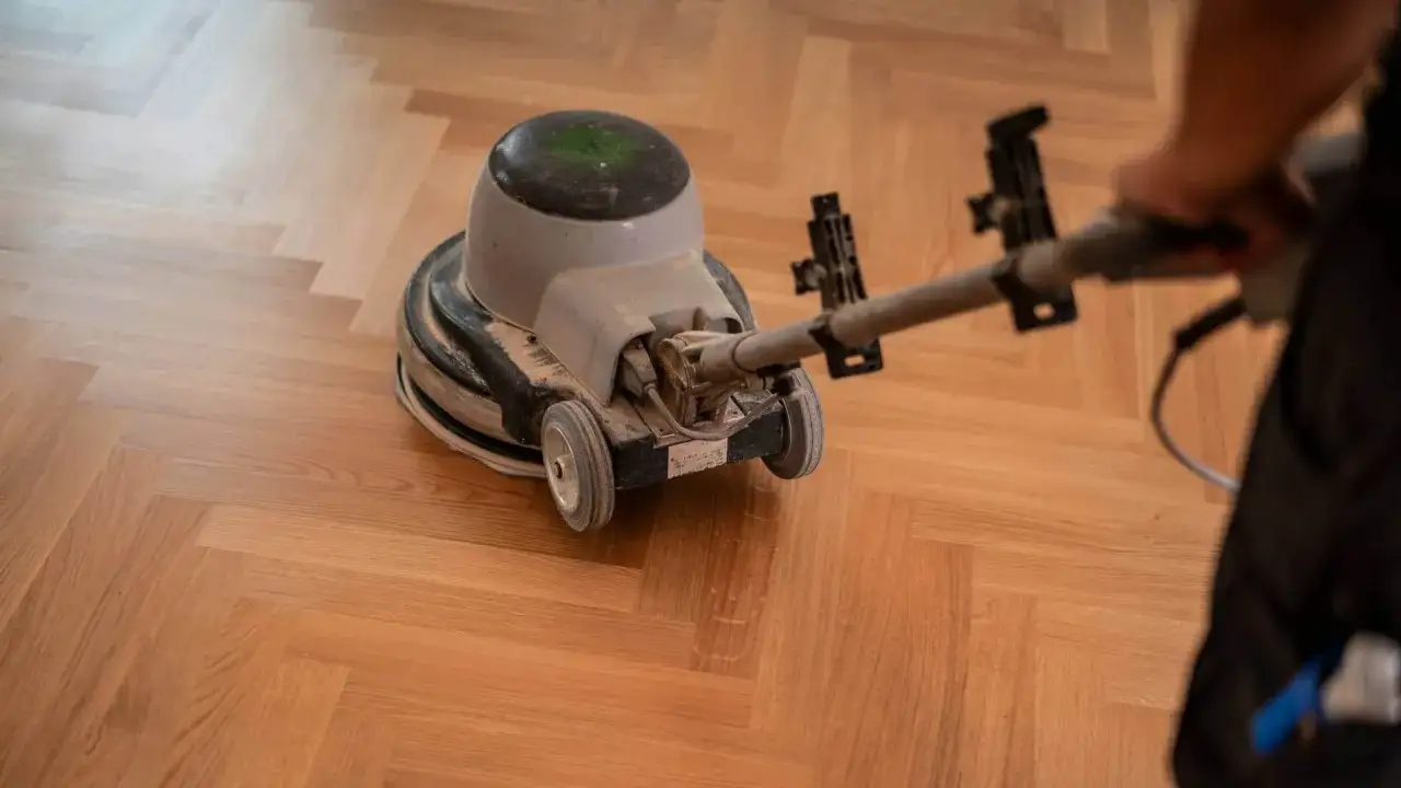 Samodzielne cyklinowanie parkietu. Maszyna szlifuje drewnianą podłogę w jodełkę, przywracając jej blask.