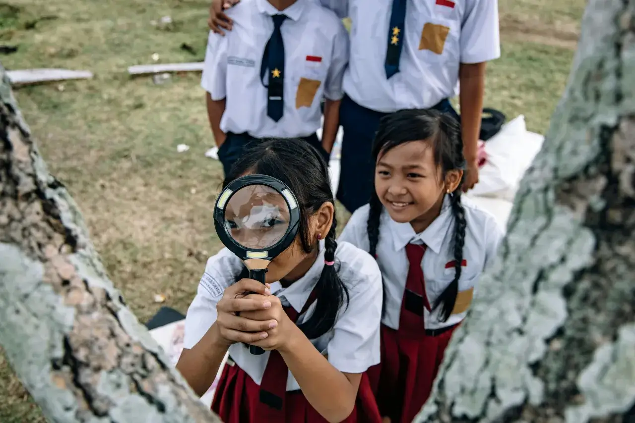 Dzieci w szkolnych mundurkach badają przyrodę przez lupę. Czy nauczyciel geografii może uczyć przyrody? Tak, gdy pokazuje świat w powiększeniu!