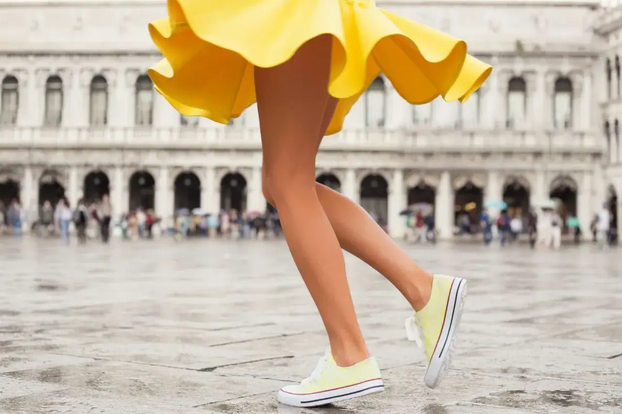 Nogi w żółtej sukience i stylowe buty sportowe do sukienki na mokrym placu w Wenecji.