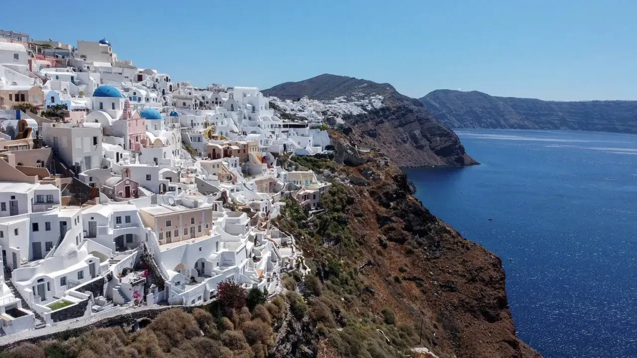 Białe domy Santorini na klifie, z błękitnymi kopułami kościołów, nad lazurowym morzem. Krajobraz jak po trzęsieniu ziemi, ale pełen życia.
