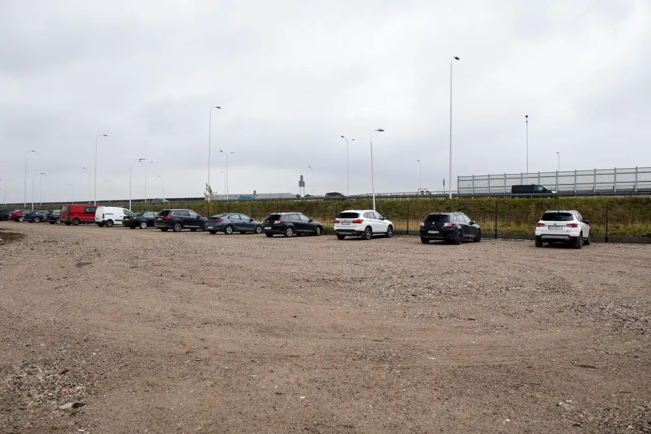 Rząd samochodów na parkingu, w tym czerwony van i białe SUV-y. Zastanawiasz się, ile kosztuje parking na lotnisku w Warszawie?