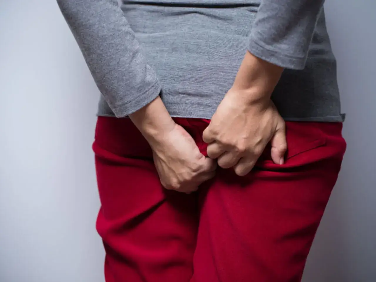 Osoba w czerwonych spodniach i szarej bluzce drapie się w okolicy odbytu. Szuka ulgi, zastanawiając się, czym smarować odbyt przy owsikach.