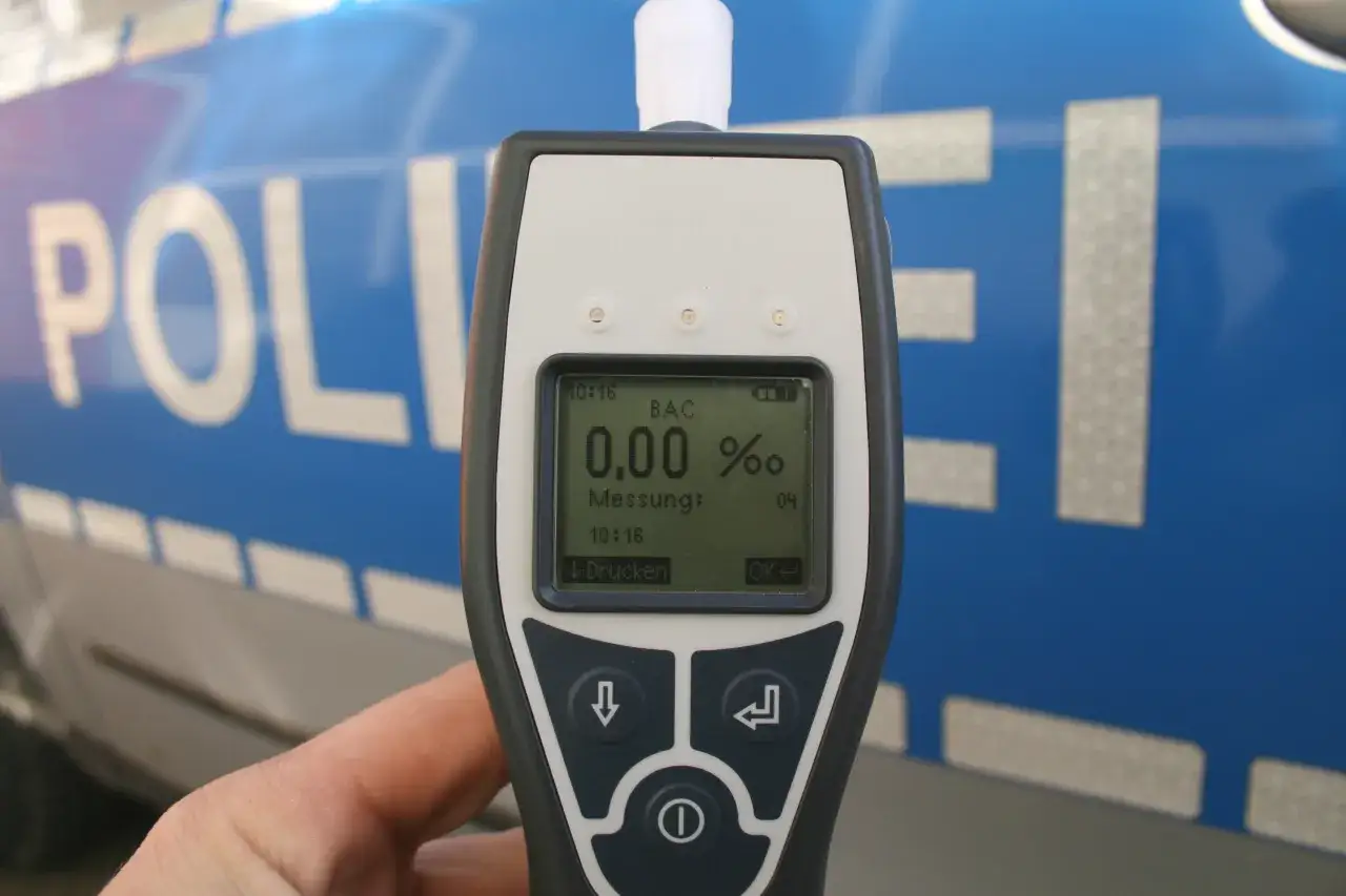 Alkomat w ręce na tle niebieskiego radiowozu policyjnego z napisem "POLIZEI".