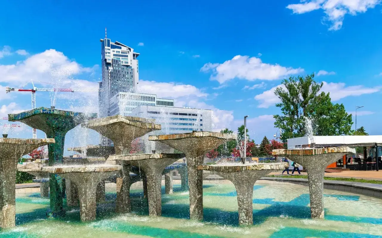 Fontanna z modernistycznymi budynkami w tle i błękitnym niebem.