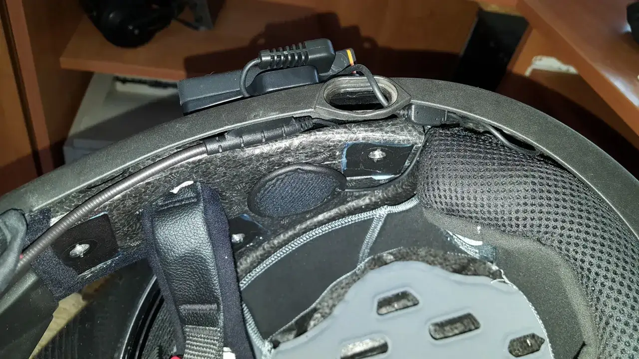Montaż interkomu w kasku motocyklowym. Widoczne przewody i moduł komunikacyjny.
