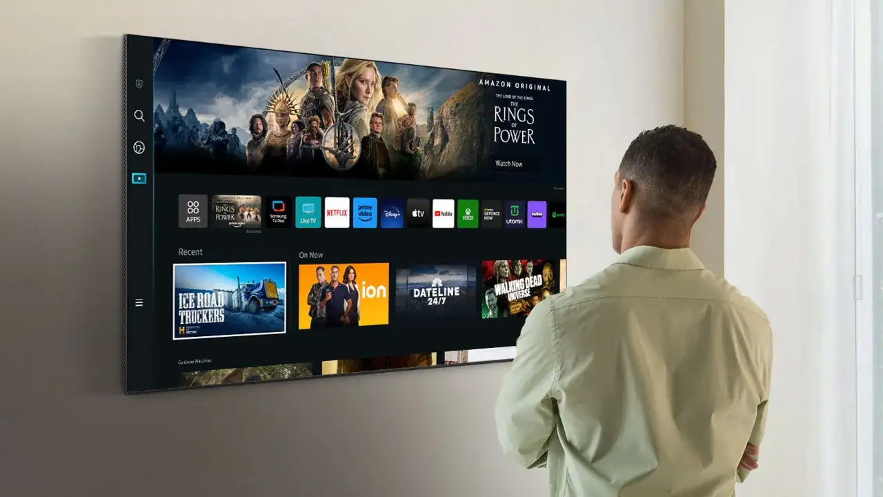 Mężczyzna patrzy na ekran telewizora Samsung Smart TV, gdzie wyświetlane są aplikacje i filmy. Dowiedz się, jak zaktualizować telewizor Samsung Smart TV, aby cieszyć się najnowszymi funkcjami.