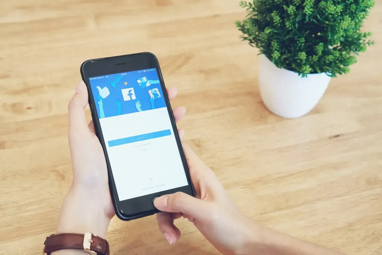 Dłoń trzymająca smartfon z ekranem logowania Facebooka.
