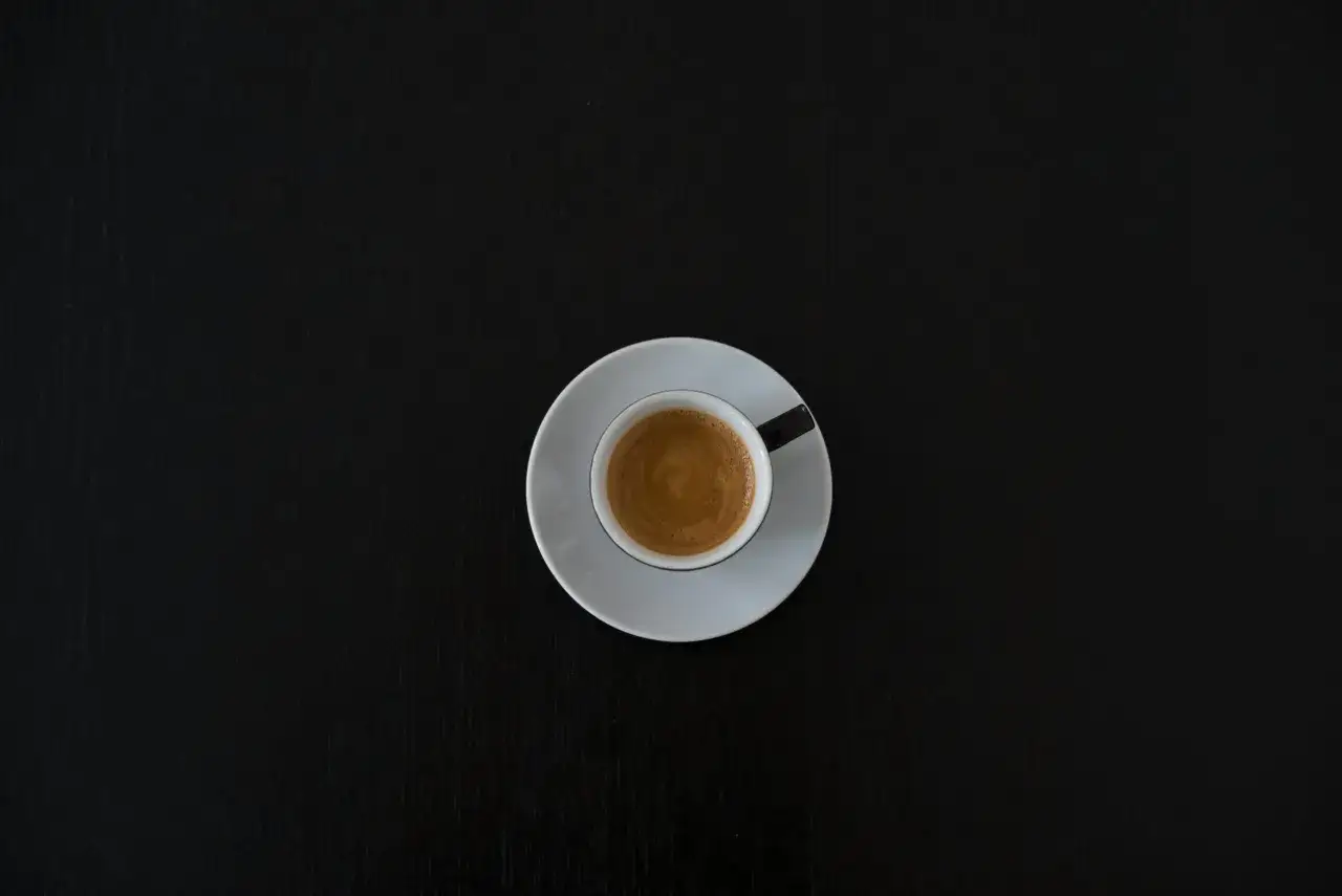 Czarna filiżanka espresso na białym spodeczku na ciemnym tle. Może symbolizować początek walki z objawami odstawienia kofeiny.