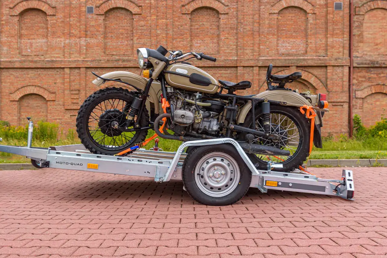 Solidne mocowanie motocykla do transportu na przyczepie. Pomarańczowe pasy zabezpieczają pojazd przed przesuwaniem.