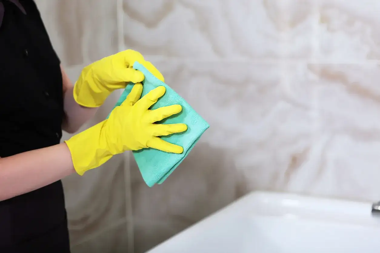 Osoba w żółtych rękawiczkach trzyma zieloną ściereczkę.