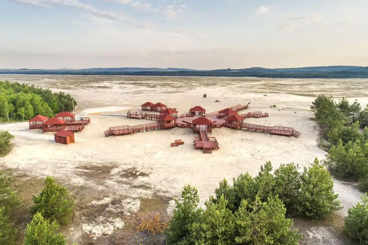 Pustynia Błędowska z widokiem na rozłożystą drewnianą konstrukcję przypominającą różę wiatrów, z altanami i pomostami.